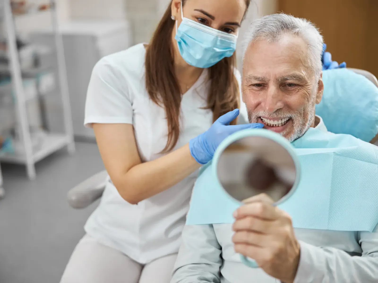 An older man looking at his new smile in a hand mirror with his dentist | Complete Smiles-Cottonwood Heights-Mountain View-Redwood-Utah